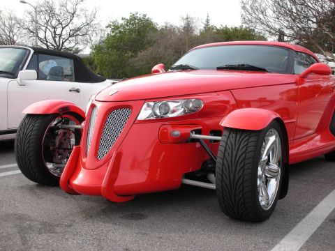 1998 Ford Crown Victoria - red Prowler-style roadster with open front wheels and exposed suspension is parked at an outdoor car meet next to a white roadster.