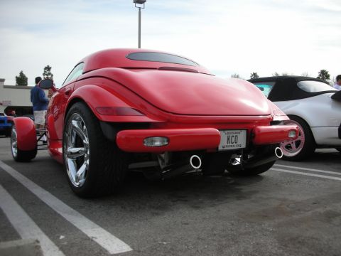 1998 Ford Crown Victoria - Rear of a red retro roadster showing curved bodywork, dual chrome exhaust tips and a Louisiana 'KCO' license plate in a parking lot.