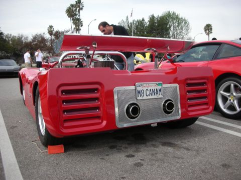1998 Ford Crown Victoria - Rear of a red mid-engine sports-racing car with engine cover propped open and a California 'M8 CANAM' license plate at a car meet.