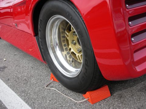 1998 Ford Crown Victoria - Close-up of a red race car's gold-centered polished alloy wheel and race tire, with an orange wheel chock on the pavement.