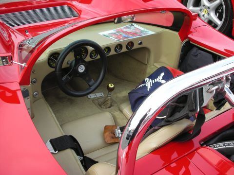 1998 Ford Crown Victoria - Interior of a red sports-racing car shows a tan cockpit with small steering wheel, row of gauges, wood shift knob and harness belts.