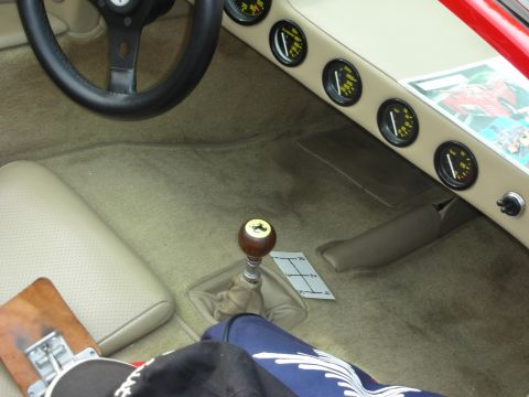 1998 Ford Crown Victoria - View into a race car's tan cockpit footwell showing the wood-knob shifter, gauge cluster and lower steering wheel.