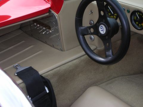 1998 Ford Crown Victoria - Close interior view of a red race car shows a black GT-marked steering wheel, riveted aluminum panel, gauges and a tan seat.