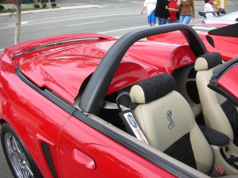 1998 Ford Crown Victoria - Tan-and-black seats of a red convertible behind a roll bar, the headrests bearing a coiled-cobra snake emblem.