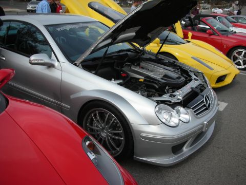 1998 Ford Crown Victoria - silver Mercedes-Benz CLK-class AMG sits with its hood raised showing the engine, flanked by red and yellow sports cars at a meet.