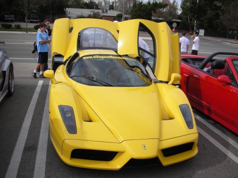 1998 Ford Crown Victoria - yellow Ferrari Enzo sits with both butterfly doors raised at an outdoor car show, onlookers and a red convertible beside it.