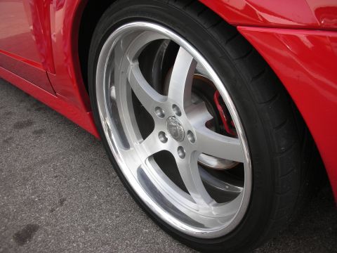 1998 Ford Crown Victoria - Close-up of a polished silver multi-spoke alloy wheel and low-profile tire on a red sports car parked on asphalt.