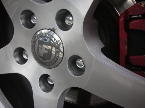 1998 Ford Crown Victoria - Macro shot of a polished five-spoke wheel's center cap and lug nuts with a red brake caliper and rotor visible behind.