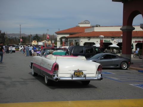 1998 Ford Crown Victoria - Rear view of a white-and-pink 1950s American convertible with chrome tailfins parked outside a strip mall at a car meet.