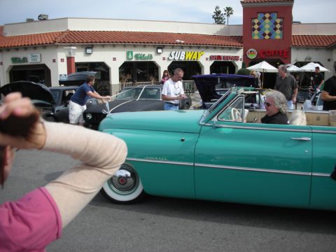 1998 Ford Crown Victoria - teal 1950s convertible with whitewall tires sits among a crowd at a strip-mall car meet near a Subway sign.