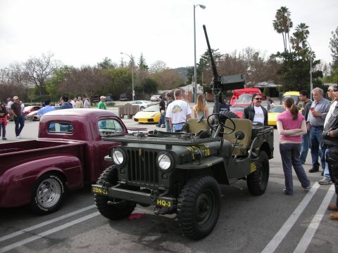1998 Ford Crown Victoria - olive-drab military Willys-style Jeep with a mounted gun sits next to a maroon vintage pickup at a car meet.