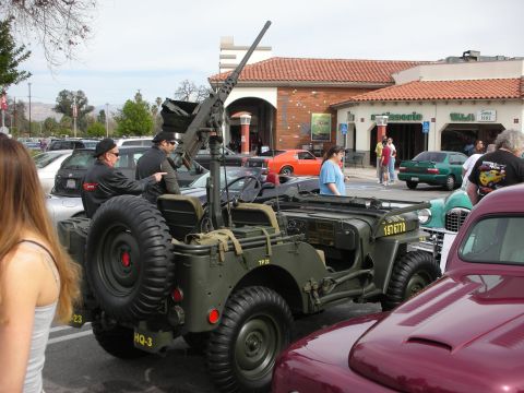 1998 Ford Crown Victoria - Rear view of an olive-drab military Jeep with a tall mounted machine gun and stacked spare tires at a car meet.