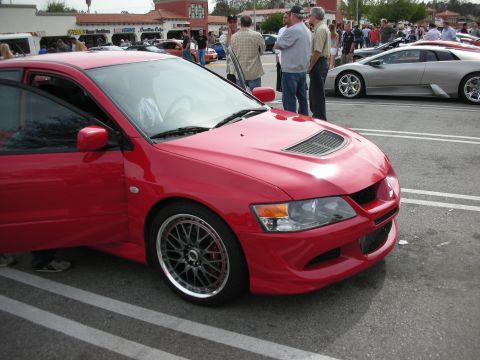 1998 Ford Crown Victoria - Front three-quarter of a red Mitsubishi Lancer Evolution showing its hood vents and dark multi-spoke wheels at a busy car meet.