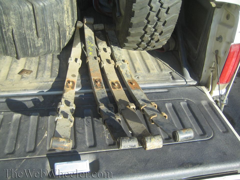 Leaf springs with yellow markings in a truck bed next to a tire
