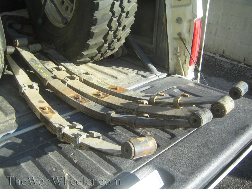 Leaf springs and bushings piled in the bed of a pickup truck next to a large tire