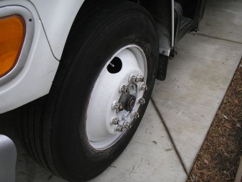1999 Ford F-800 - Close-up of the front wheel assembly on a white truck, showing dual tires and a white-painted hub.
