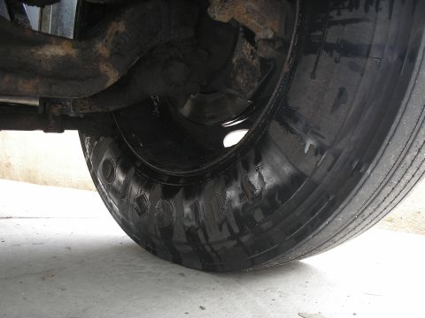1999 Ford F-800 - Close-up of a medium-duty truck's front wheel with a Firestone highway-rib tire on a steel wheel, both glistening with fresh black paint or…