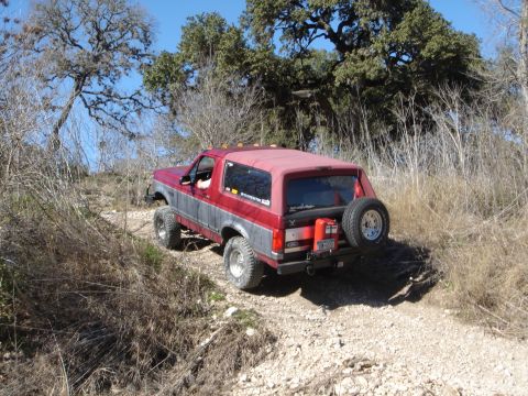 1995 Ford Bronco - 1995 Ford Bronco navigating an off-road trail with a spare tire and gas can mounted on the rear.