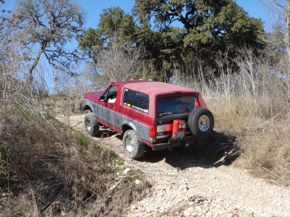 Red and gray Ford Bronco with rear tire carrier on a rocky brush trail