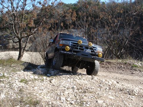 1995 Ford Bronco - A lifted Ford truck navigates a rough, off-road path with sparse vegetation.