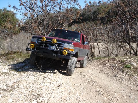 1995 Ford Bronco - A red and grey Ford Bronco is parked on a rocky, dirt path with trees in the background.