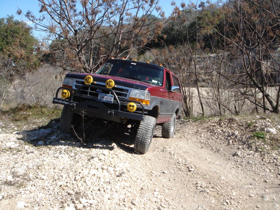 Red and grey Ford Bronco with KC lights and smiley face mud flaps on a dirt road