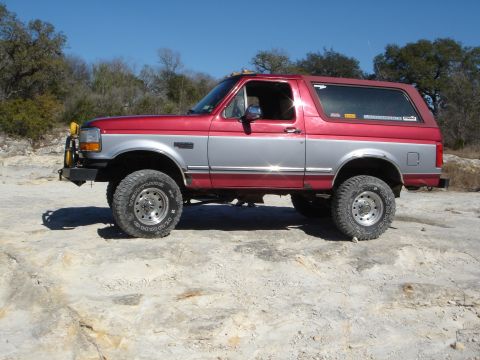 1995 Ford Bronco - Side profile of a two-tone red and silver Ford Bronco off-road.