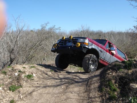 1995 Ford Bronco - A red and gray Ford F-series truck navigates a steep, dirt trail with a clear blue sky above.
