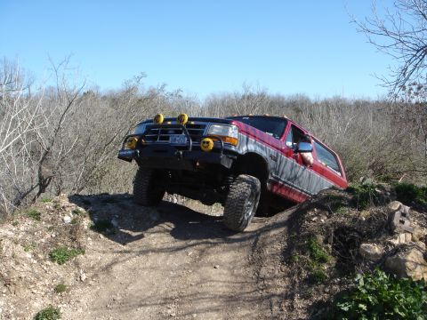 1995 Ford Bronco - A red and grey Ford Bronco navigates a steep, rocky incline under a clear blue sky.