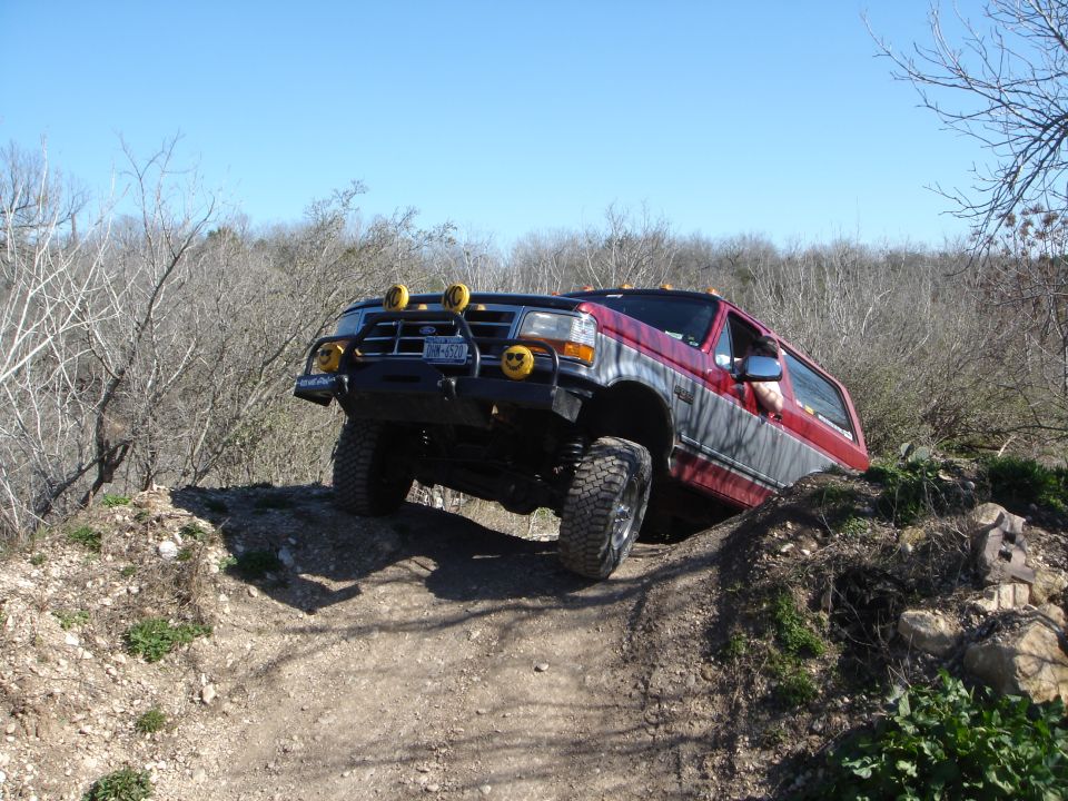 Lifted red and gray Ford SUV flexed on a rocky off-road trail with brush guard and light bar