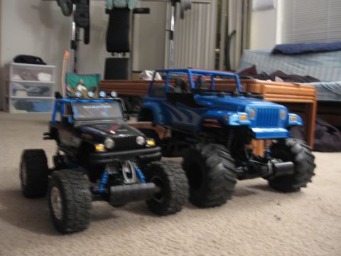 1990 Ford Bronco - Two remote-controlled monster trucks are positioned on a carpeted floor inside a room.