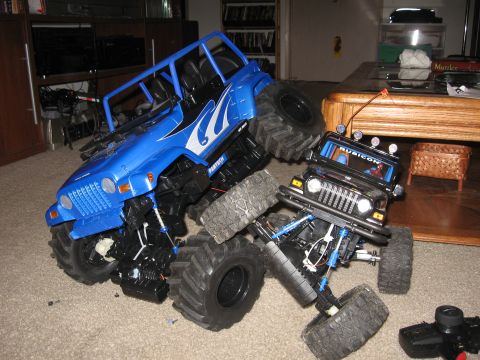 1990 Ford Bronco - Two remote-controlled monster trucks are stuck on each other in a living room setting.