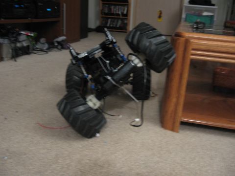 1990 Ford Bronco - A remote control monster truck lies on its side indoors, showing its complex suspension and large off-road tires.