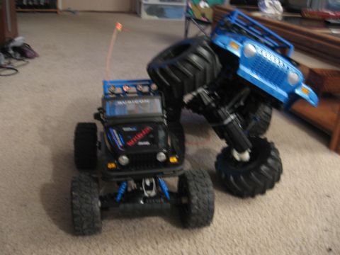 1990 Ford Bronco - Two RC monster trucks are positioned on a carpeted floor, with one appearing to be climbing over the other.