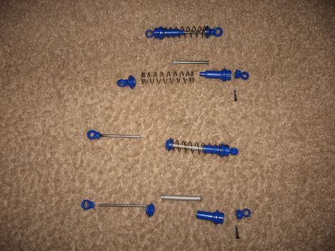 1990 Ford Bronco - Several blue shock absorber assemblies and their components are spread out on a carpeted surface.
