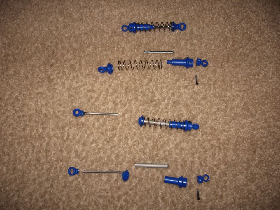 Disassembled blue shock absorbers and related parts laid out on carpet
