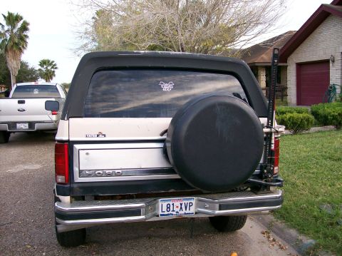 1981 Ford Bronco - Rear view of a tan Ford Bronco with a spare tire mounted on the back, parked on a street.