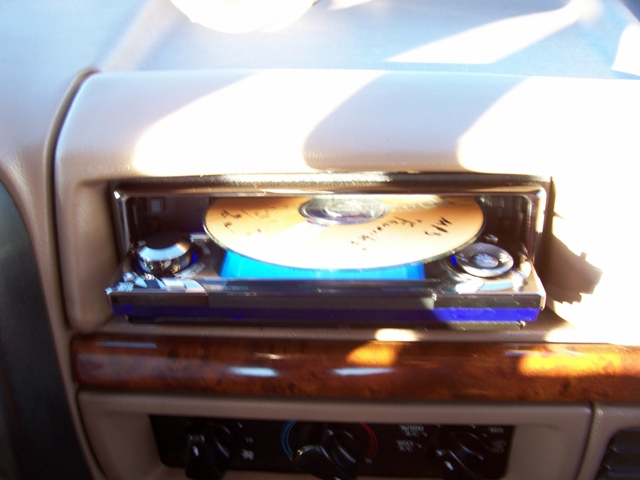 Car's CD player with a CD inside, showing some writing on it. Wood trim and climate controls visible below