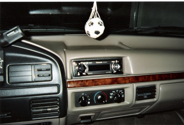 Tan dashboard interior with aftermarket stereo and wood trim. A soccer ball air freshener hangs from the rearview mirror