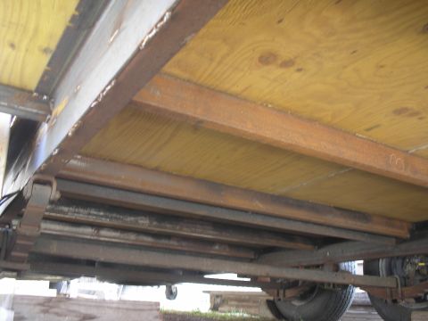 1990 Ford Bronco - Underside view of a flatbed trailer or truck bed showing plywood decking over rusty steel cross-members and channel frame rails. A multi-le…