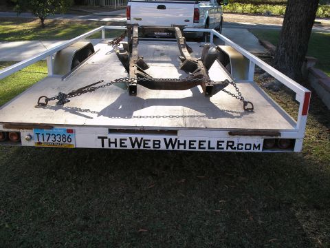 1990 Ford Bronco - Trailer loaded with a vehicle chassis, parked in front of a white pickup truck.