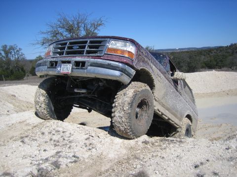 1986 Ford Bronco - This lifted Ford F-Series truck is stuck in the mud, its front end angled upwards.