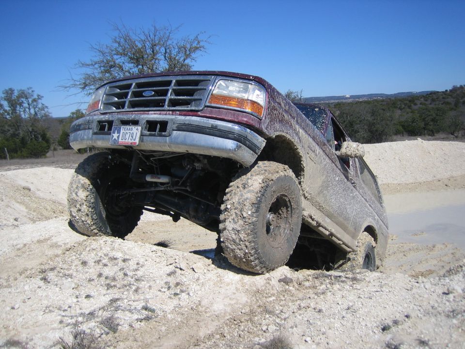 Maroon Ford F-Series truck with lifted suspension stuck in mud, front 3/4 view