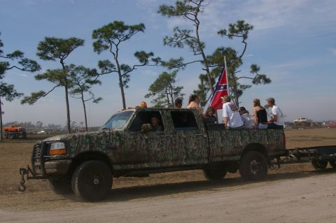 1974 Ford F-100 - A group of people ride in the bed of a camouflaged pickup truck, with a Confederate flag flying.