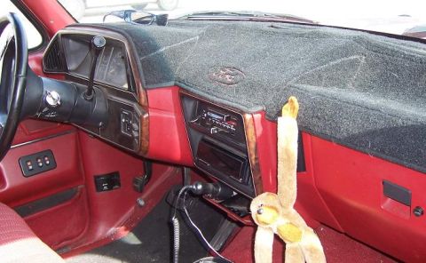 1991 Ford Bronco - The interior of a red vehicle is shown, the dashboard, steering wheel, and a plush monkey toy hanging from the vent.