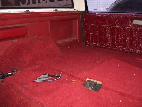 1991 Ford Bronco - The rear interior of a vehicle shows worn red carpeting and exposed trim components.