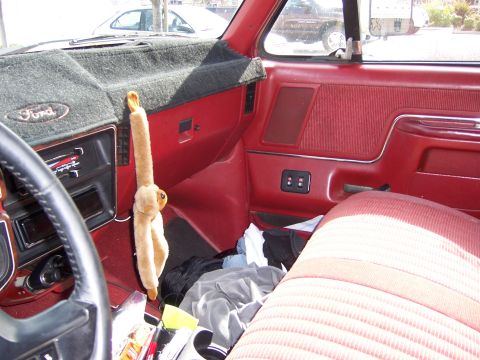 1991 Ford Bronco - The interior of a 1991 Ford Bronco shows a red dashboard, seats, and door panels, with a stuffed animal hanging from the gear shift.