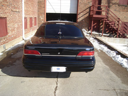 1992 Ford Crown Victoria - Rear view of a black 1992 Ford Crown Victoria parked outside a garage.