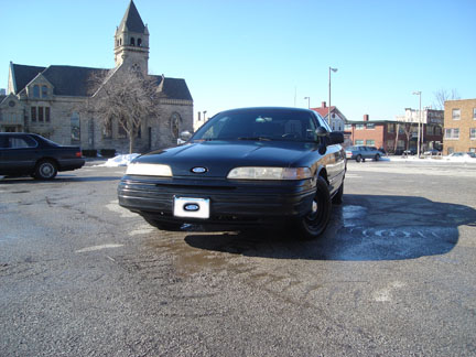 1992 Ford Crown Victoria - A black 1992 Ford Crown Victoria is parked in a lot with another car and a building in the background.