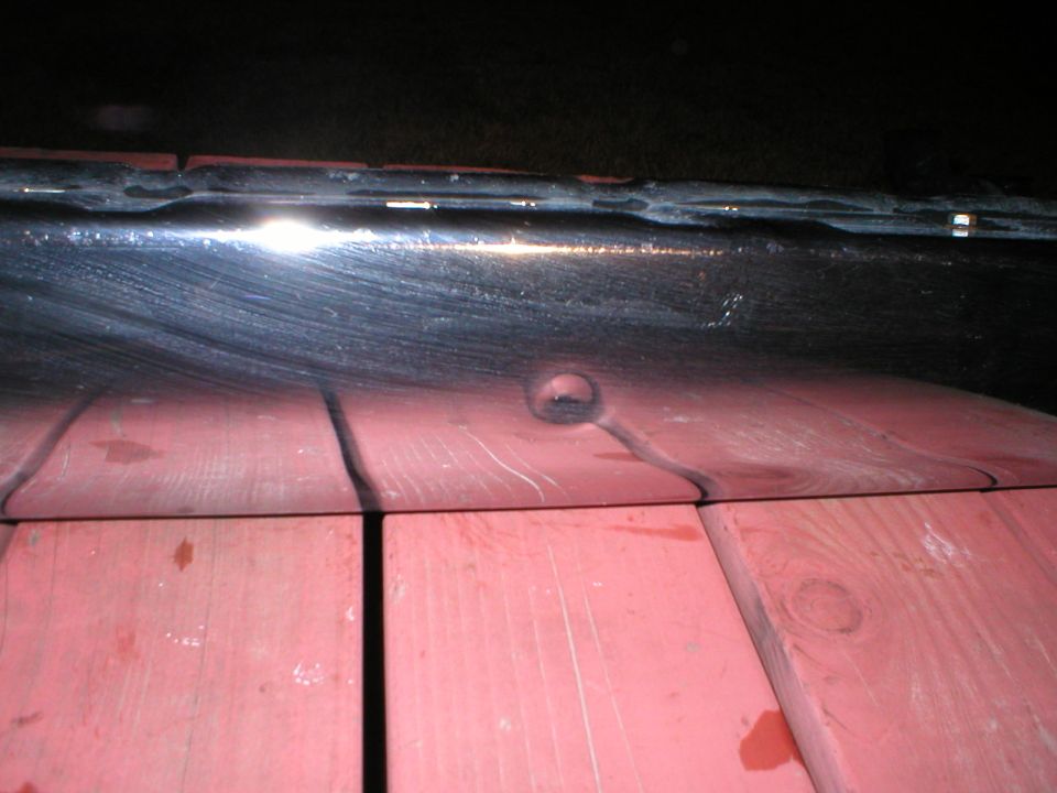 Black vehicle bumper with a circular dent, resting on red wooden planks